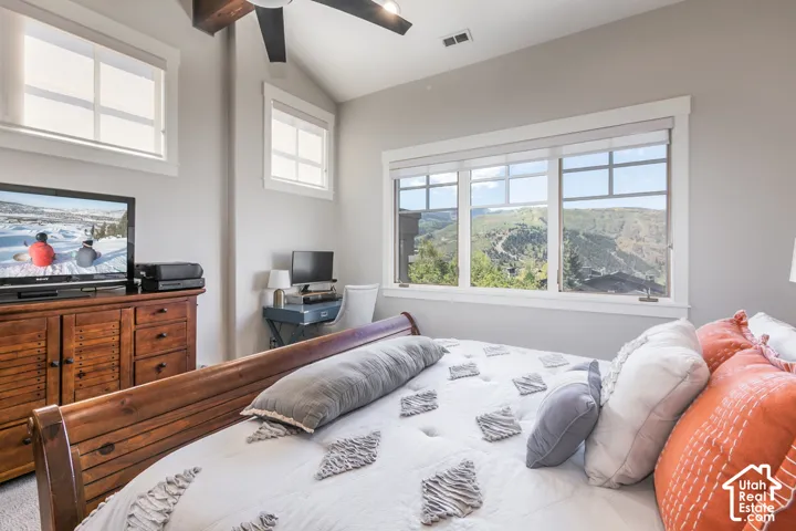 Vaulted ceiling with exposed wood beam, ceiling fan, multiple windows with mountain scenery, and light gray wall color