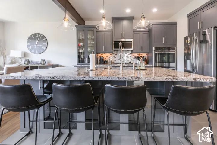 Expansive kitchen island with a stone countertop, featuring pendant lighting, integrated stainless steel appliances, and gray cabinetry