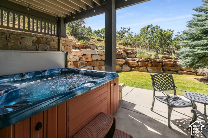 Covered patio featuring a built-in hot tub, concrete paving, and a stone retaining wall