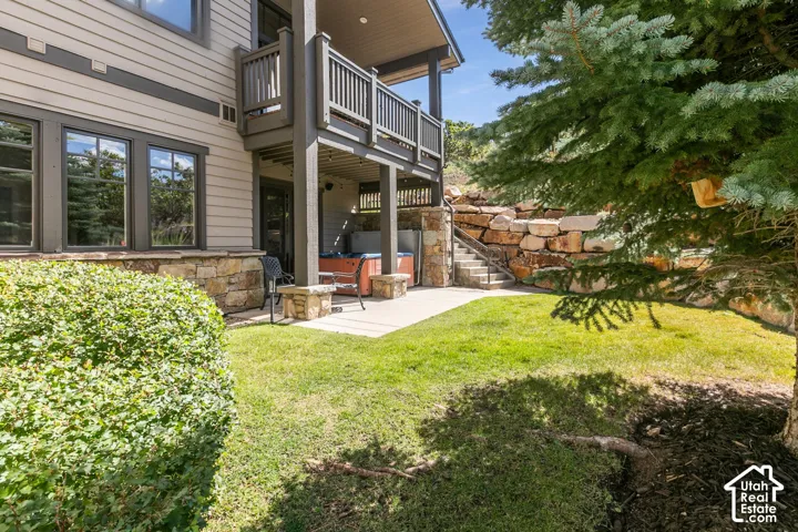 Private patio featuring a built-in hot tub, stone retaining wall, staircase, and a covered balcony