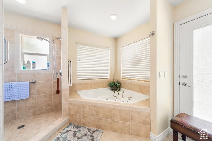 Tile-surround corner soaking tub with multiple jets, walk-in shower with tile surround, and a glass-paneled door
