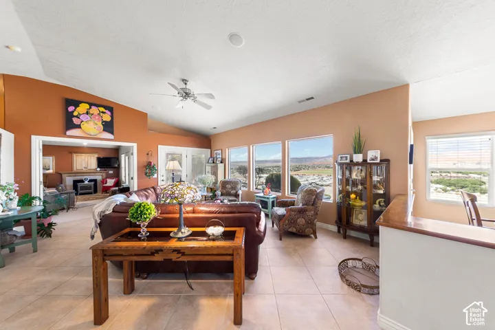 Vaulted ceilings with a ceiling fan, multiple windows, and light-toned tile flooring
