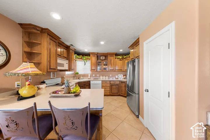 Kitchen featuring wood cabinetry, stainless steel refrigerator, white countertops, recessed lighting, and tile flooring