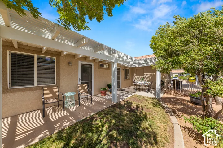 Rear patio with a white pergola, stucco exterior, and mature trees