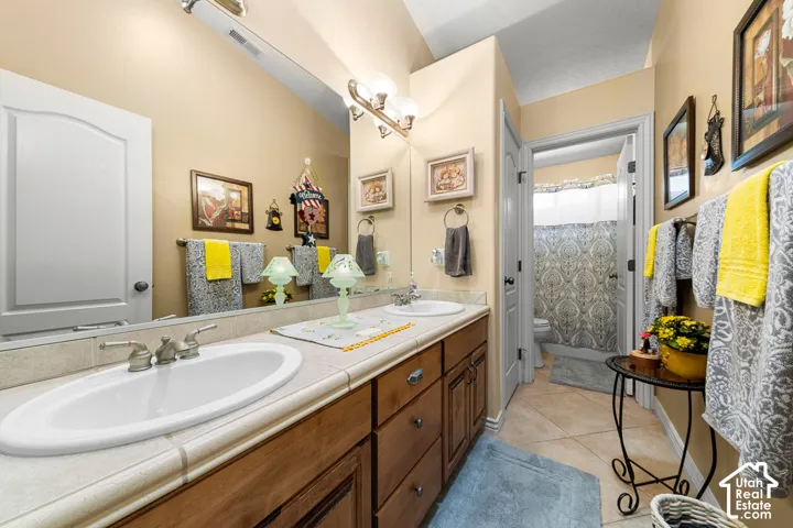 Dual vanity with undermount sinks, tile countertop, wood-finish cabinetry, and brushed nickel fixtures