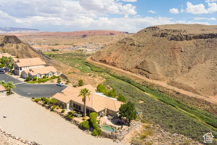 Terracotta tile roof home with an integrated pool and spa, surrounded by desert landscaping, with a prominent desert canyon backdrop featuring a riverbed