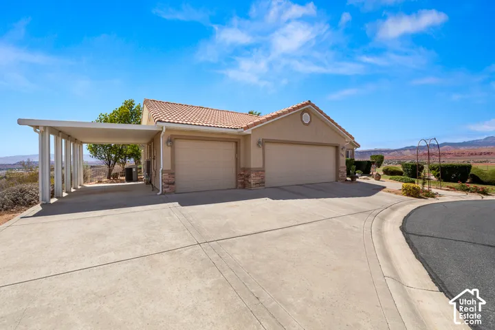 Stucco exterior with a tile roof, dual garage doors, a covered carport, and a concrete driveway