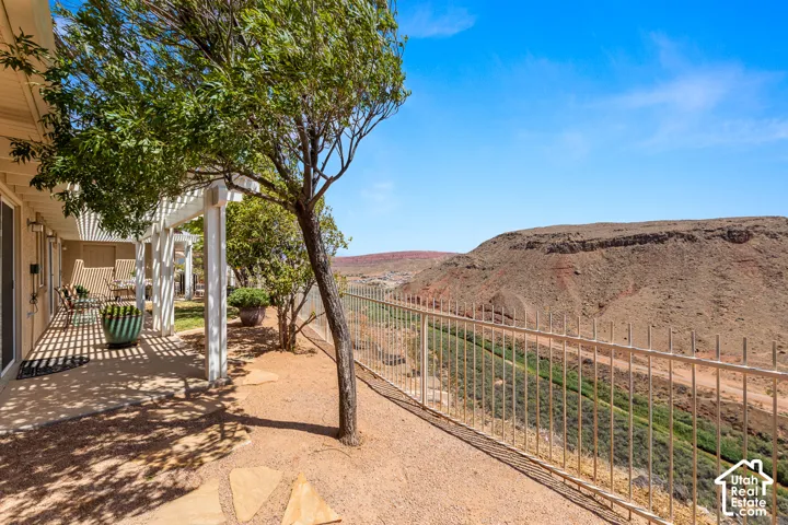 Pergola-covered patio with desert landscaping, a decorative metal fence, and distant natural rock formations