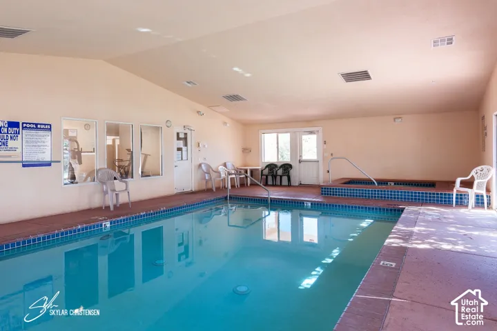 Indoor swimming pool with blue tiled perimeter, integrated hot tub, and multiple windows