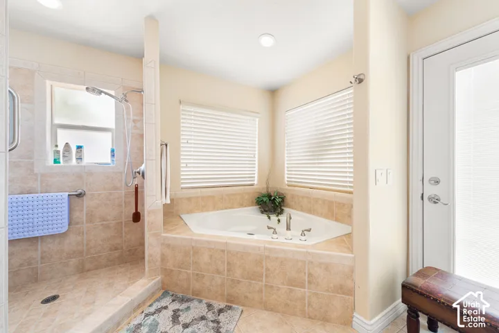 Tile-surround corner soaking tub with multiple jets, walk-in shower with tile surround, and a glass-paneled door
