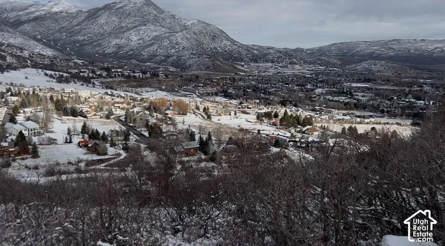 Expansive mountain landscape featuring snow-dusted peaks, distant residential structures, and a valley setting