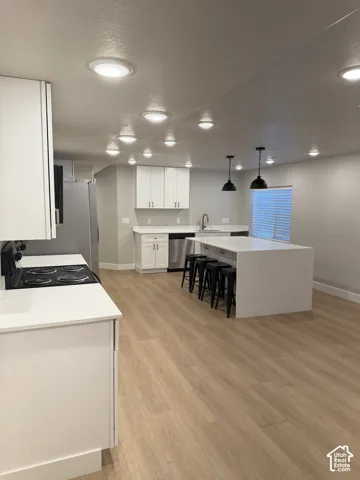 Kitchen featuring white cabinetry, light-toned wood-finish flooring, recessed lighting, a kitchen island with seating, and stainless steel appliances