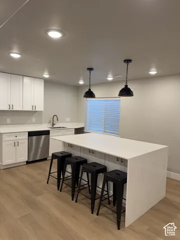 Kitchen featuring white shaker cabinetry, stainless steel appliances, light-toned wood-finish flooring, and a waterfall island with pendant lighting