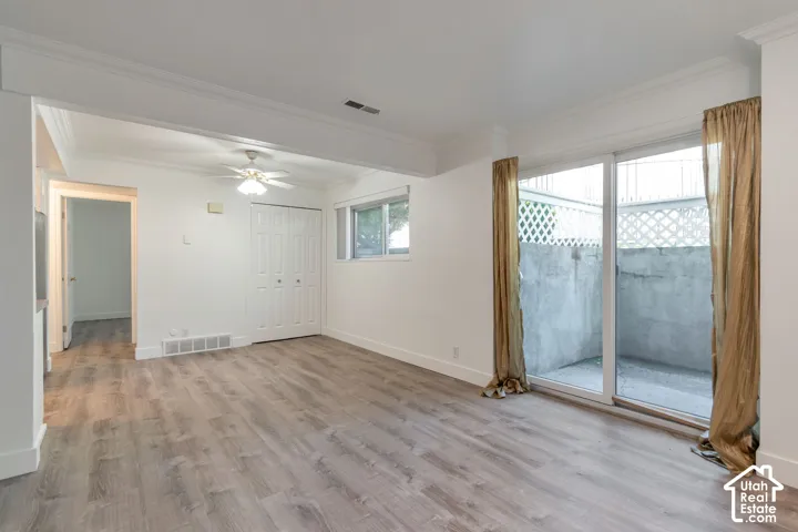 Spacious room featuring wood-finish flooring, white walls, and crown molding