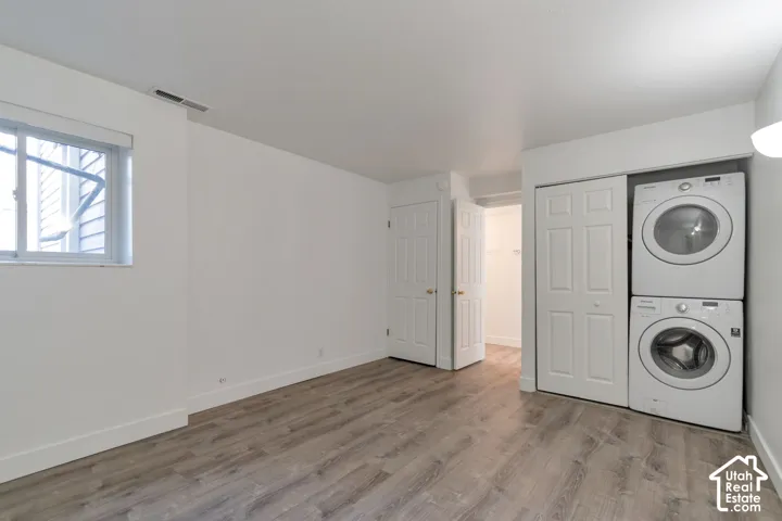 Laundry area featuring stacked washer and dryer appliances, wood-finish flooring, and white walls