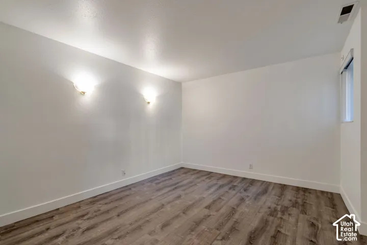 Wood-finish flooring, white painted walls, wall-mounted sconces, and a window