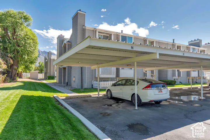 Carport parking structure with a multi-level building featuring gray siding, white trim, and various window configurations