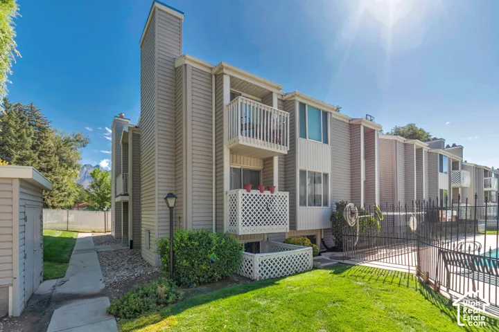 Two-story residence with light-toned siding, a second-story balcony, and a ground-level patio