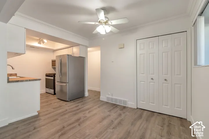 Wood-finish flooring throughout, stainless steel refrigerator and range, white bi-fold closet doors, ceiling fan with integrated lighting, and white cabinetry