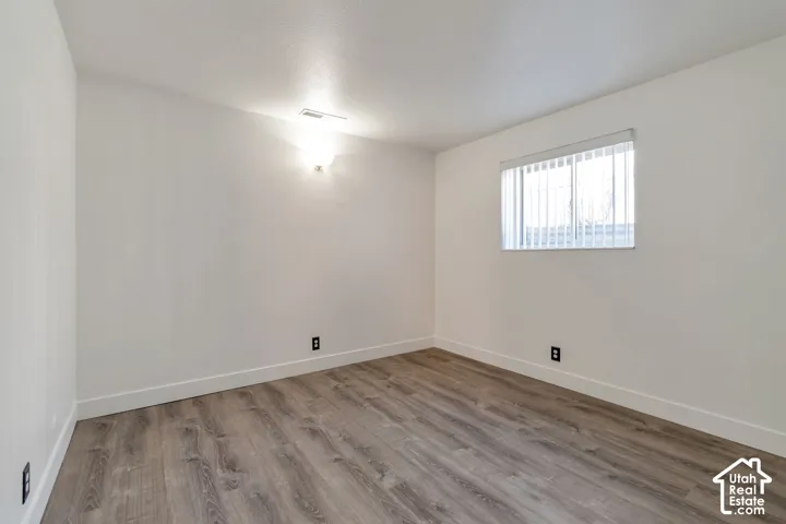 Wood-finish flooring, white walls, horizontal window blinds, and an integrated ceiling light fixture