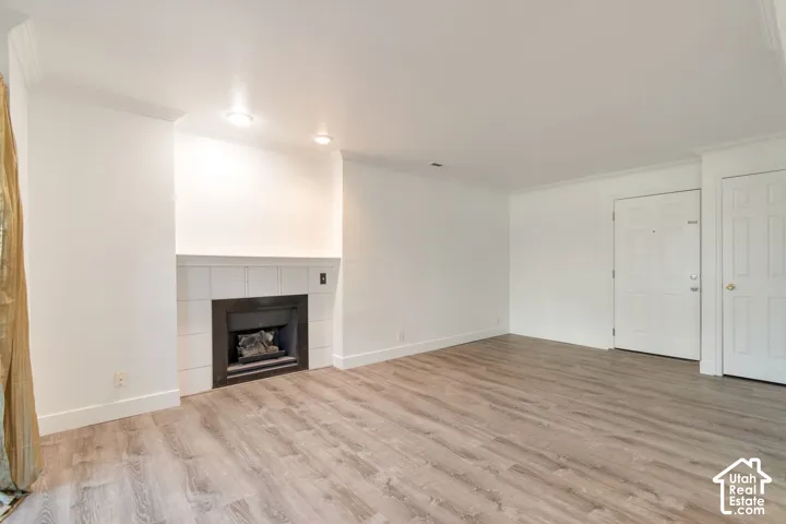 Living area featuring wood-finish flooring, a fireplace with a tiled surround, recessed lighting, and crown molding