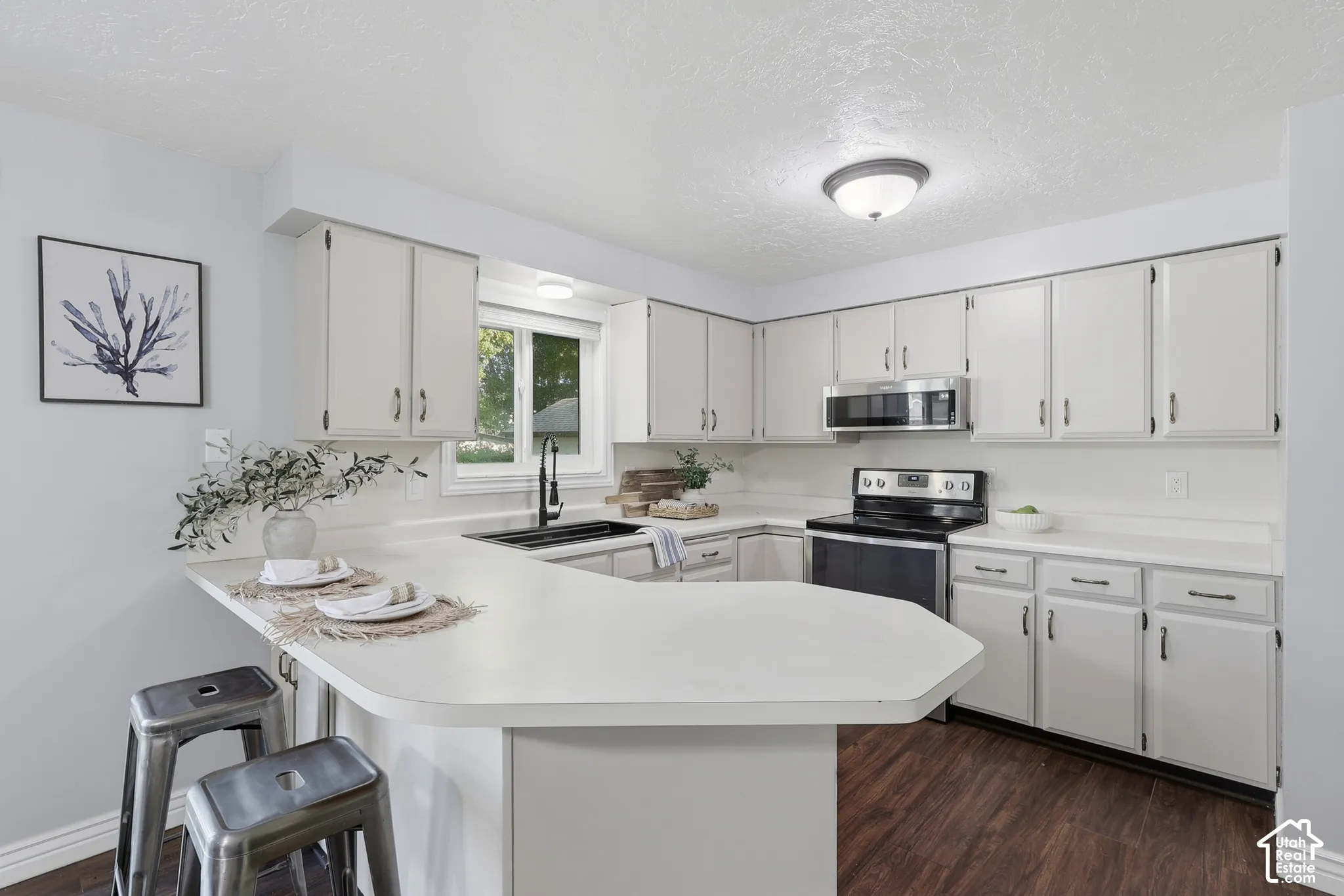 White cabinetry, white countertops, built-in microwave, dark range, and wood-finish flooring