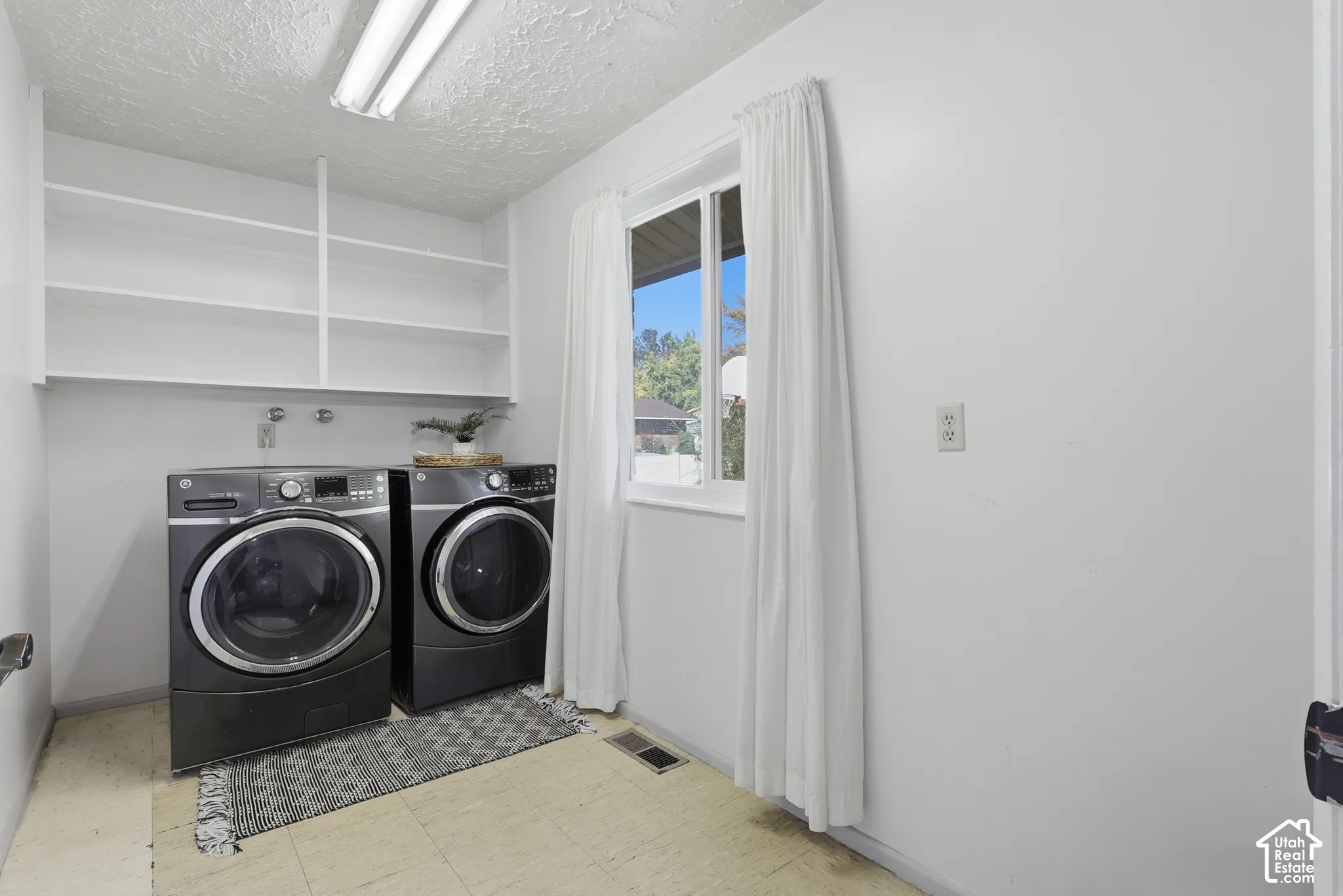 Laundry area featuring white walls, overhead shelving, and a window for natural light