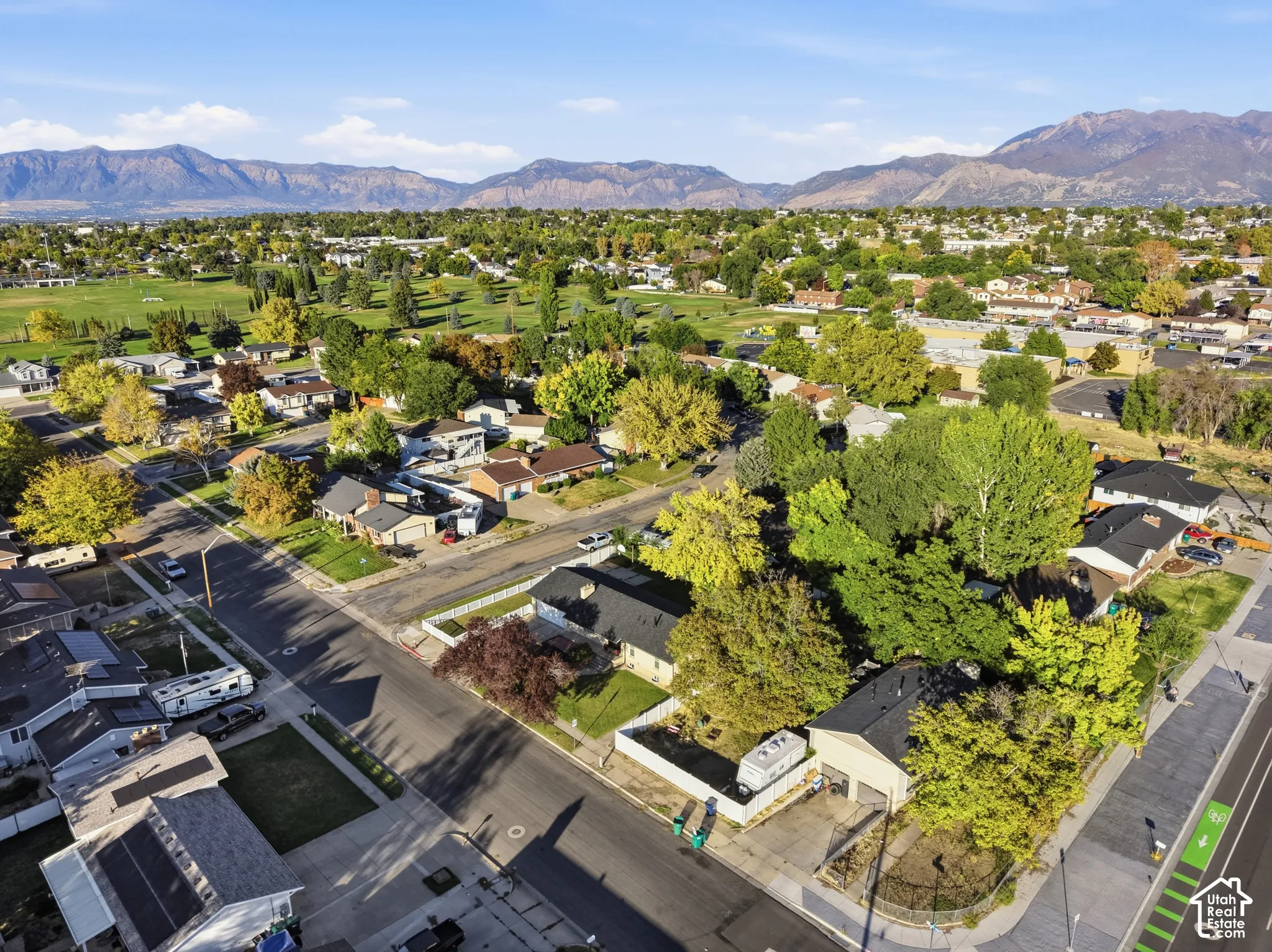 Aerial view showcasing this residential property nestled within a tree-lined neighborhood, featuring mature landscaping, ample lot size, and mountain backdrop