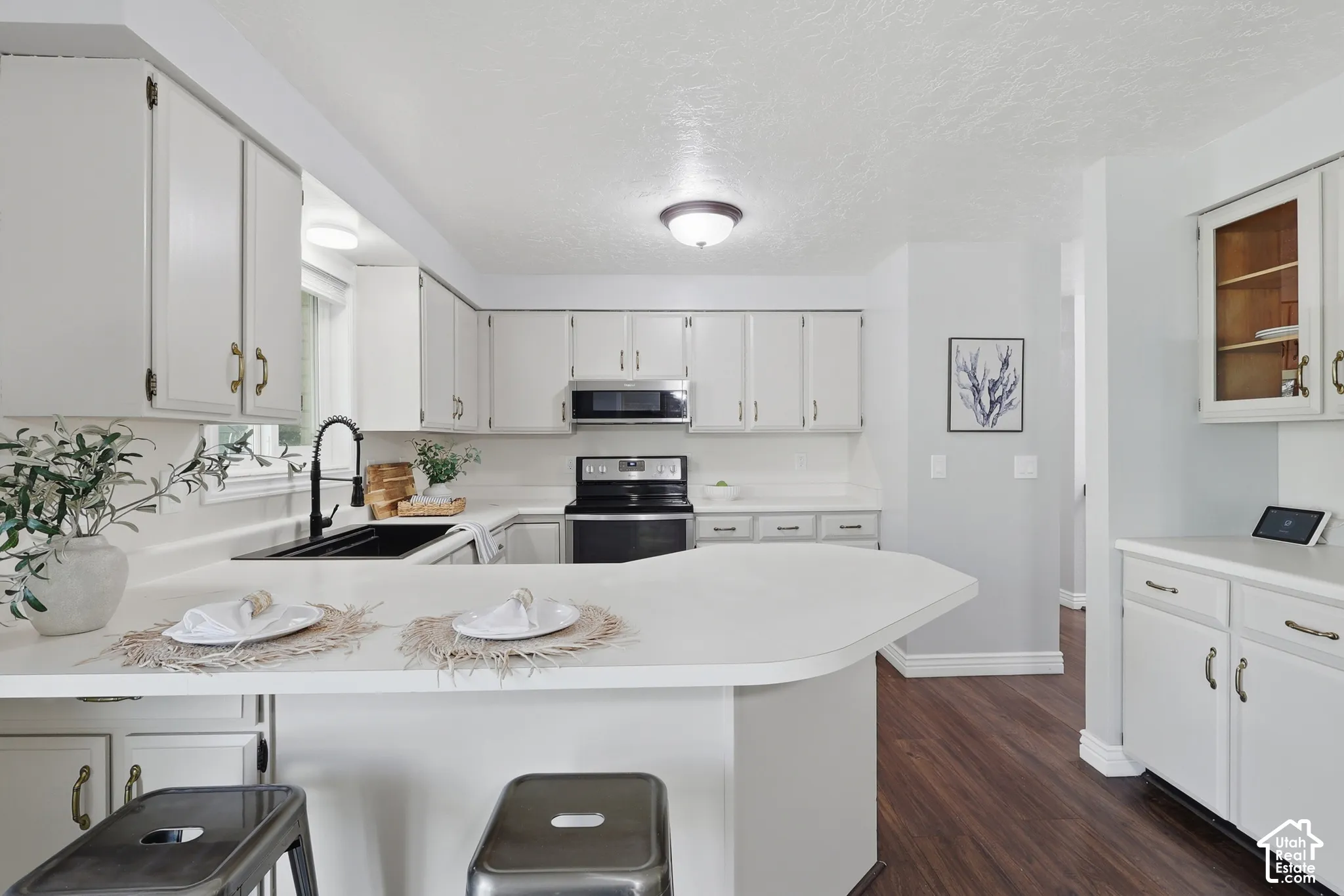 Modern kitchen featuring white cabinetry with brushed nickel hardware, a curved center island with white countertop seating, stainless steel built-in appliances, wood-finish flooring throughout, and abundant natural light from recessed ceiling fixtures