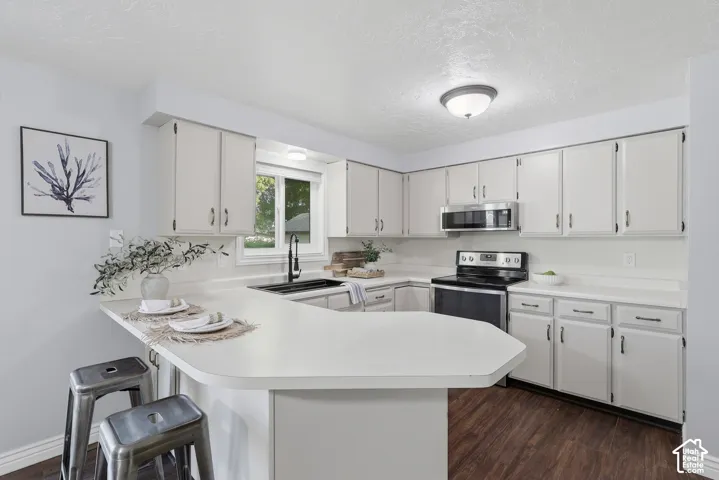 White cabinetry, white countertops, built-in microwave, dark range, and wood-finish flooring
