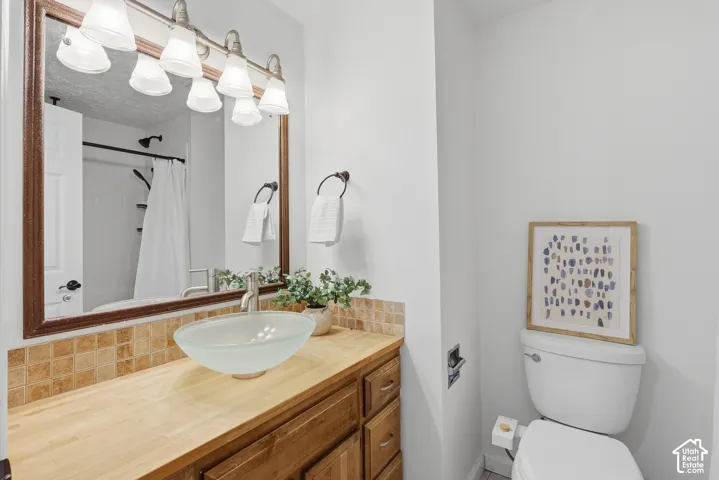Warm wood-finish vanity with a vessel sink, square tile backsplash, large framed mirror, and a three-light fixture