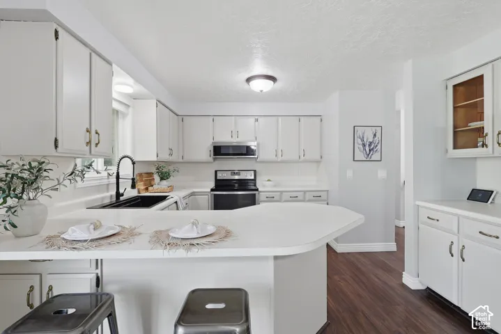 Modern kitchen featuring white cabinetry with brushed nickel hardware, a curved center island with white countertop seating, stainless steel built-in appliances, wood-finish flooring throughout, and abundant natural light from recessed ceiling fixtures