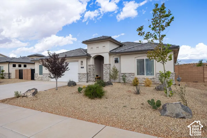 Stucco exterior with stone accents, covered entry, attached garage, tile roof, and desert landscaping
