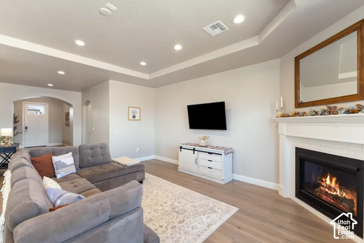 Recessed lighting, tray ceiling, fireplace with a white mantel, light wood-finish flooring, and arched doorway