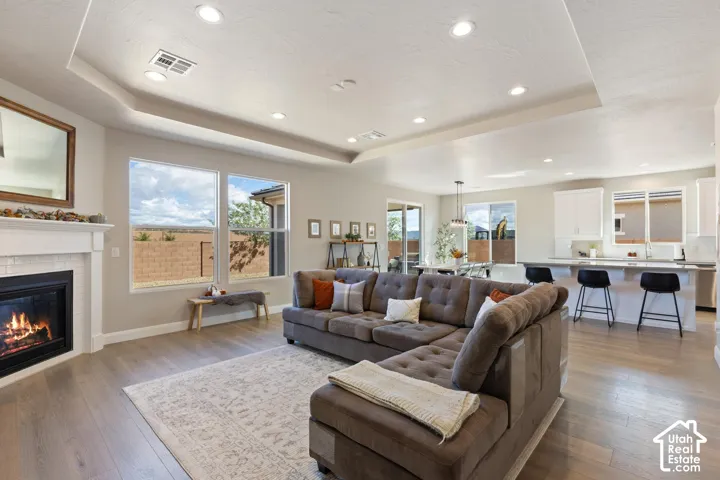 Bright open-concept living space with wood-finish flooring, a white mantel fireplace, and large windows