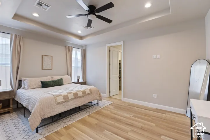 Recessed lighting, ceiling fan, tray ceiling, wood-finish flooring, and a white paneled door