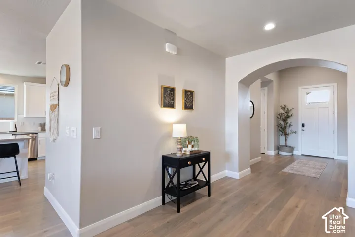 Hardwood-finish flooring extending through an arched entryway, recessed ceiling lighting, and a paneled entry door with transom window