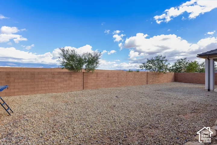 Expansive backyard featuring a gravel-covered surface, a block privacy fence, and a covered patio area