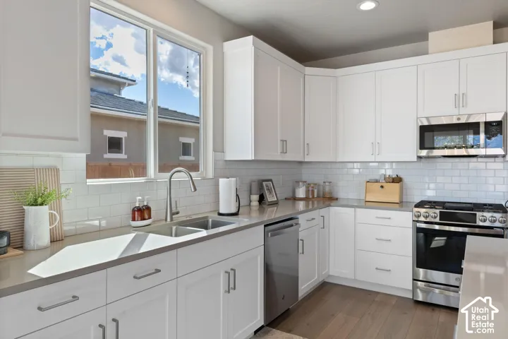 White shaker cabinetry with brushed nickel hardware, light-toned countertops, subway tile backsplash, stainless steel appliances, and wood-finish flooring