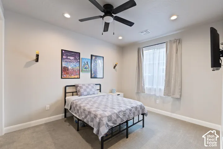Recessed ceiling lighting, ceiling fan, carpet flooring, and a window with sheer and blackout curtains