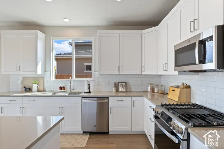 White shaker cabinetry, stainless steel appliances, subway tile backsplash, recessed lighting, and wood-finish flooring