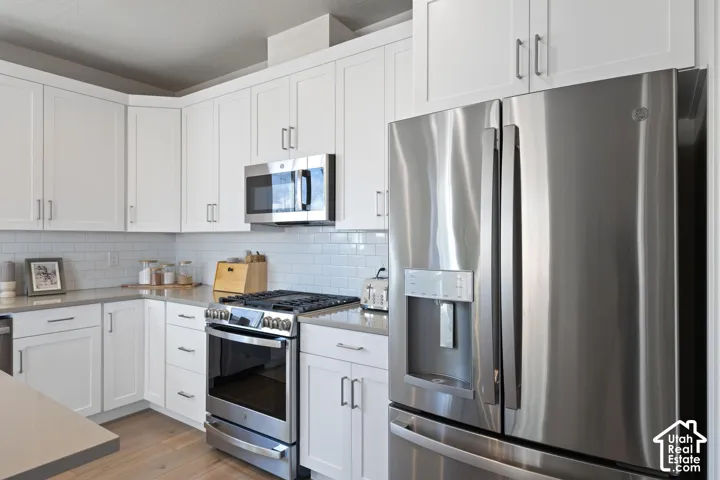 Modern kitchen featuring white cabinetry, gray countertops, stainless steel appliances, a subway tile backsplash, and wood-finish flooring