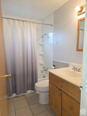 Bathroom featuring a wood-finish vanity, integrated sink, tile flooring, and a tub-shower combination with built-in shelving