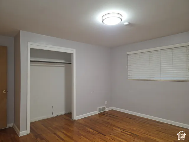 Interior space featuring wood-finish flooring, a reach-in closet with integrated shelving, and a horizontal window with adjustable blinds