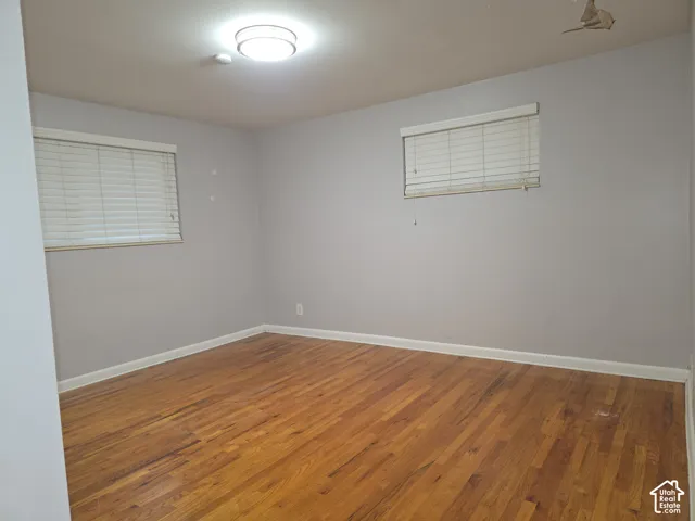 Room featuring wood-finish flooring, two windows with horizontal blinds, and a ceiling-mounted flush light fixture