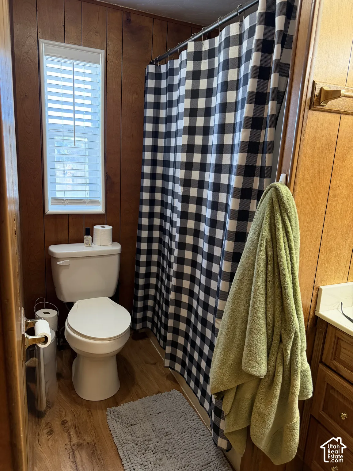 Bathroom featuring wood-finish paneling, wood-finish flooring, a white toilet, and a window with blinds