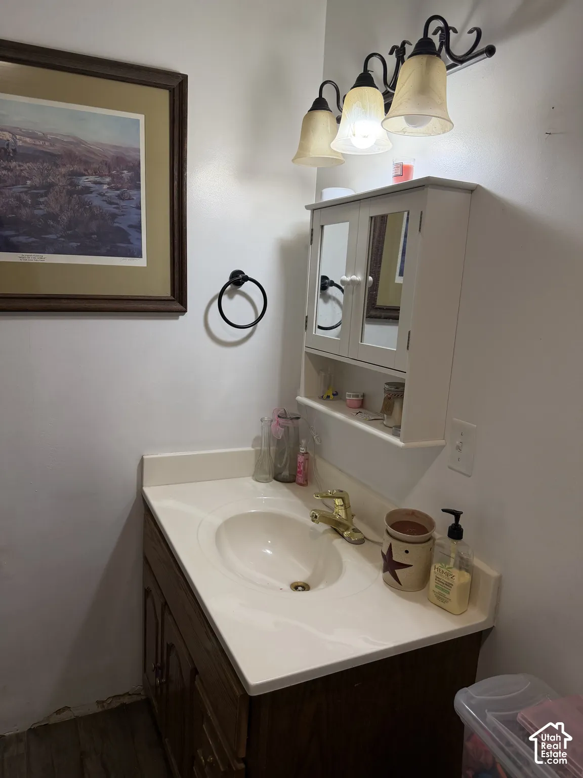 Vanity with an integrated sink and a brass-finish faucet, accompanied by a three-light fixture with bell-shaped shades