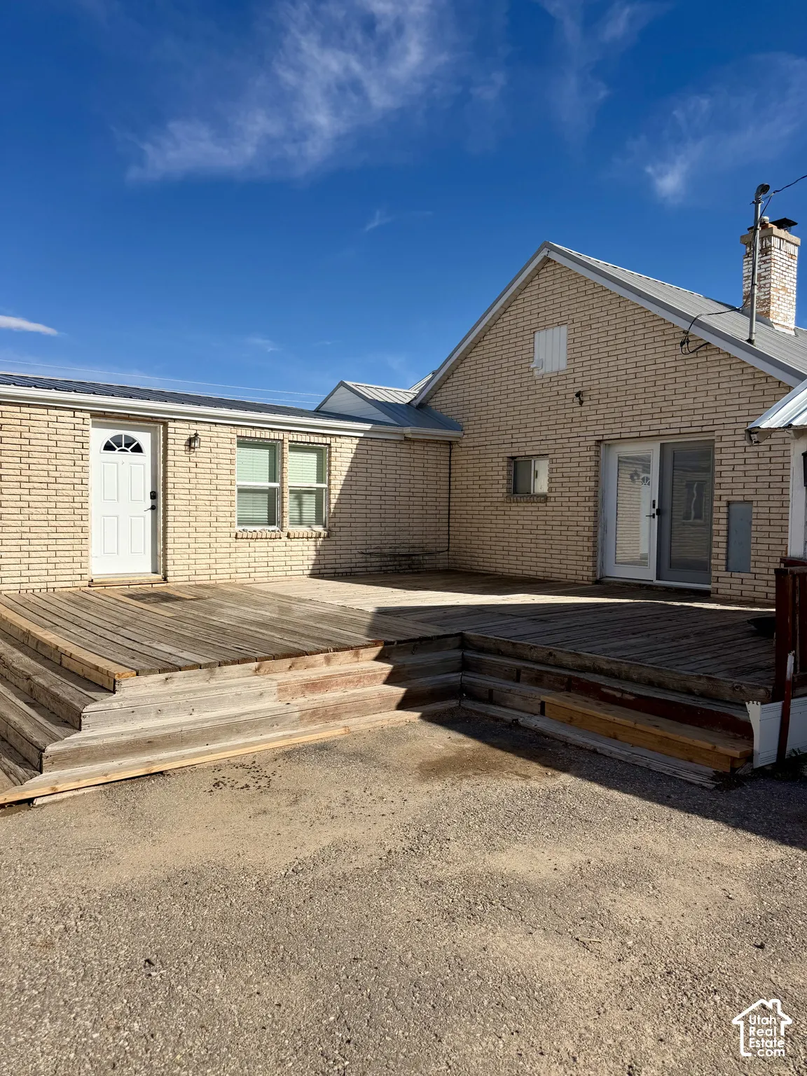 Expansive wooden deck with multi-level construction, brick exterior, sliding glass door access, and a metal roof