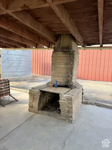 Outdoor brick-clad fireplace with a concrete patio under a wood-beamed ceiling