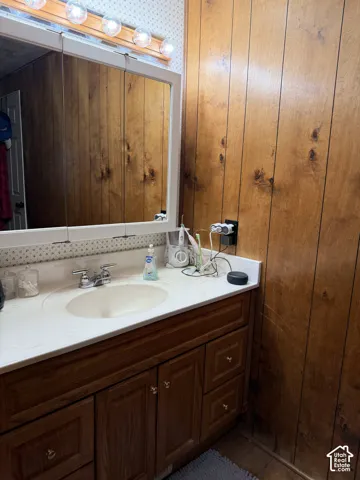 Wood-paneled wall, vanity with wood-finish cabinetry, white countertop, oval sink, and a built-in medicine cabinet with integrated lighting